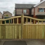 Natural wood garden gate with curved top and vertical slats, installed between stone pillars, ideal for privacy and aesthetic appeal.