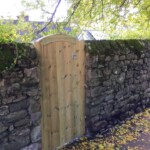 Handcrafted wooden garden gate by Richard Hope, made from durable, natural timber, providing privacy and aesthetic appeal to garden entrance, surrounded by traditional stone wall and foliage.