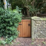 Elegant wooden garden gate by Richard Hope Wooden Gates, crafted from high-quality timber, seamlessly blends with lush greenery and rustic stone walls. Perfect for enhancing curb appeal and security.