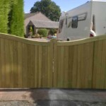 Natural wooden garden gate with a curved top, installed between brick pillars, providing privacy and security for a residential property.
